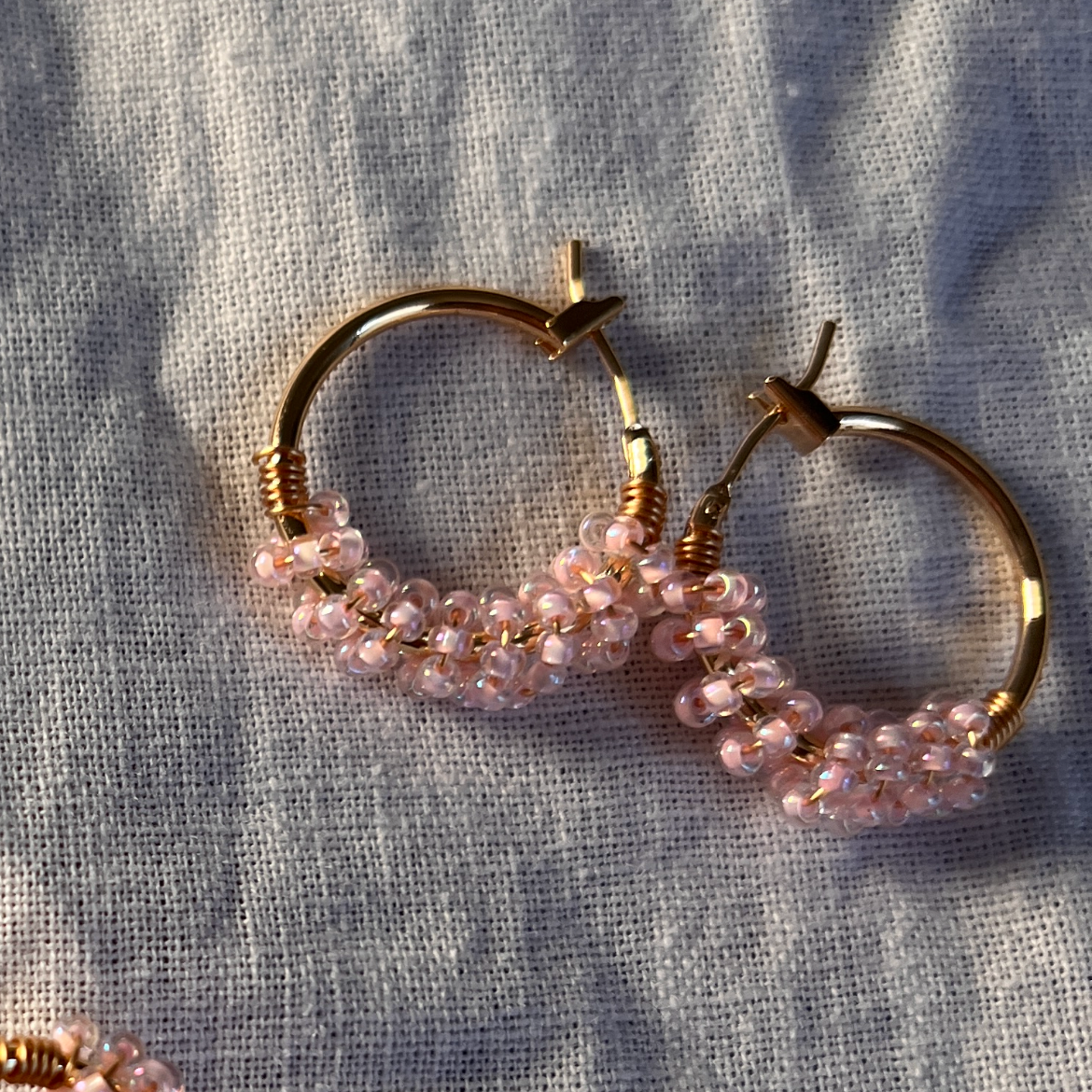 Gold hoop earrings with pink beads on a textured fabric background