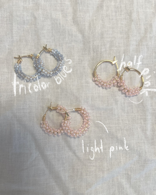 Three beaded hoop earrings labeled 'tricolor blue', 'half pink', and 'light pink' on a textured fabric background.
