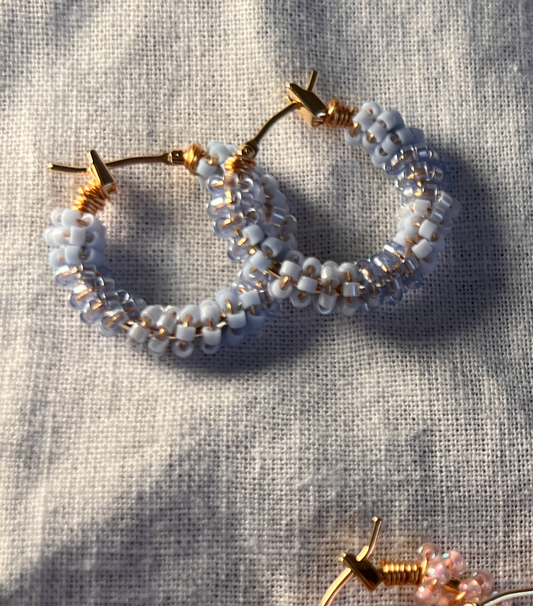 Pair of hoop earrings with pearl-like beads on a textured fabric background