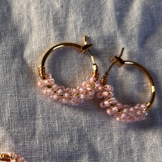 Gold hoop earrings with pink beads on a textured fabric background